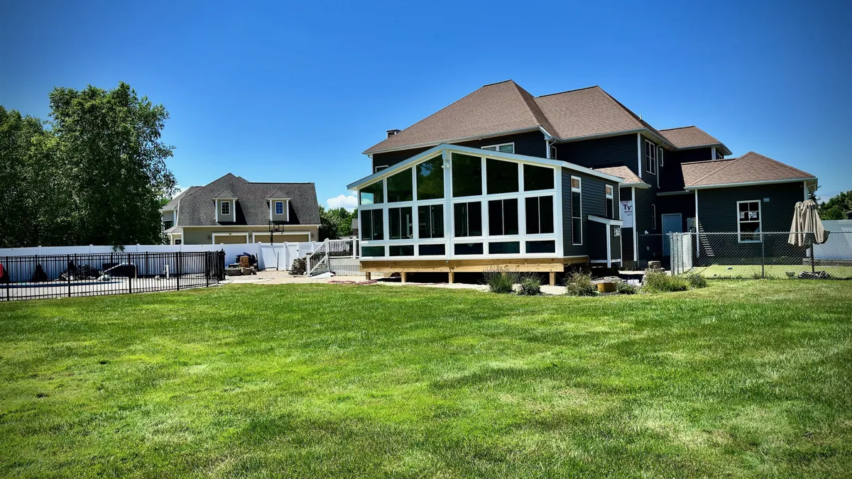 Dark-framed sunroom across the back of a home, facing a wide lawn