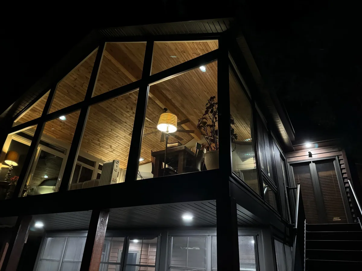 Dark-framed gable sunroom lit warmly at night