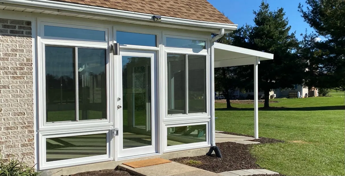 White-framed sunroom with a glass entry door opening onto the lawn