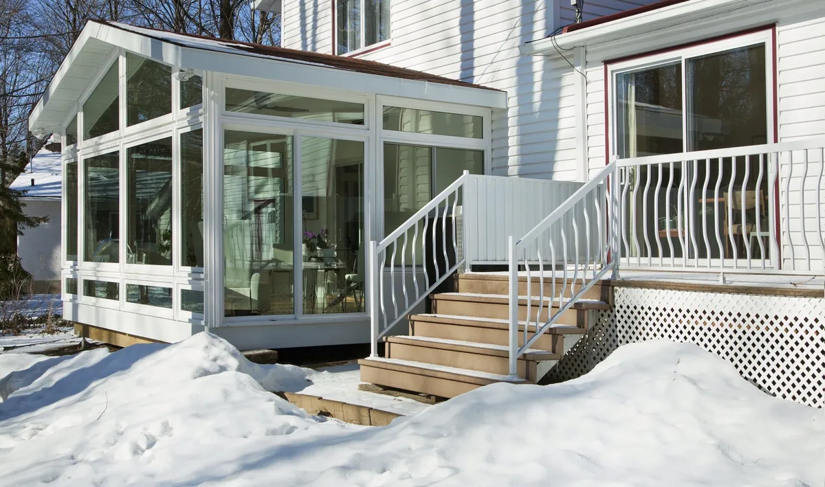 White sunroom with a curved stair rail, surrounded by winter snow
