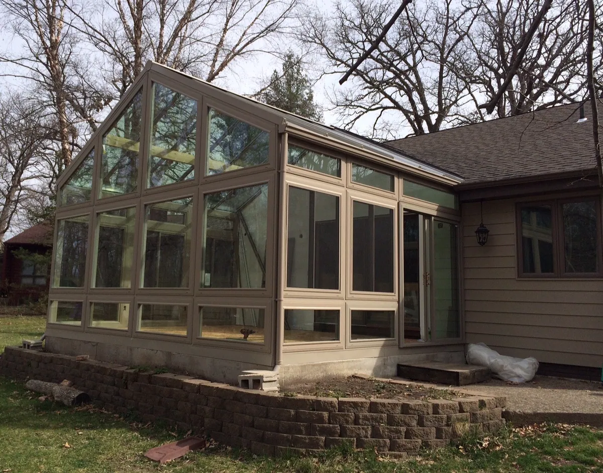 Tall gable glass sunroom against a brick home under mature trees