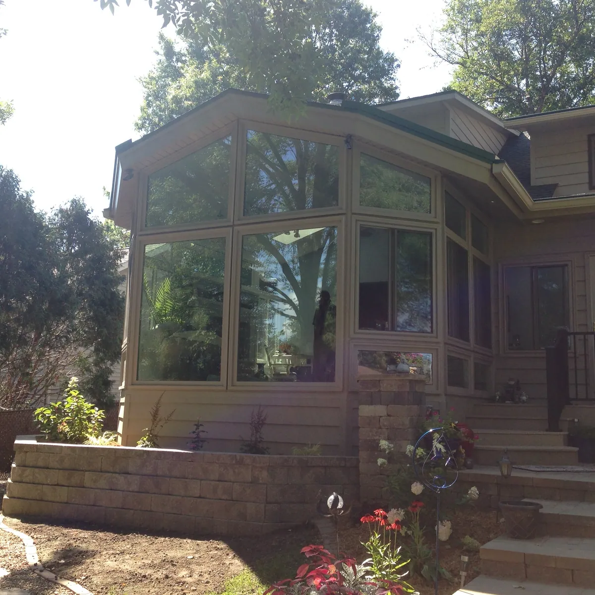 Wood-toned sunroom above stone steps in a mature garden