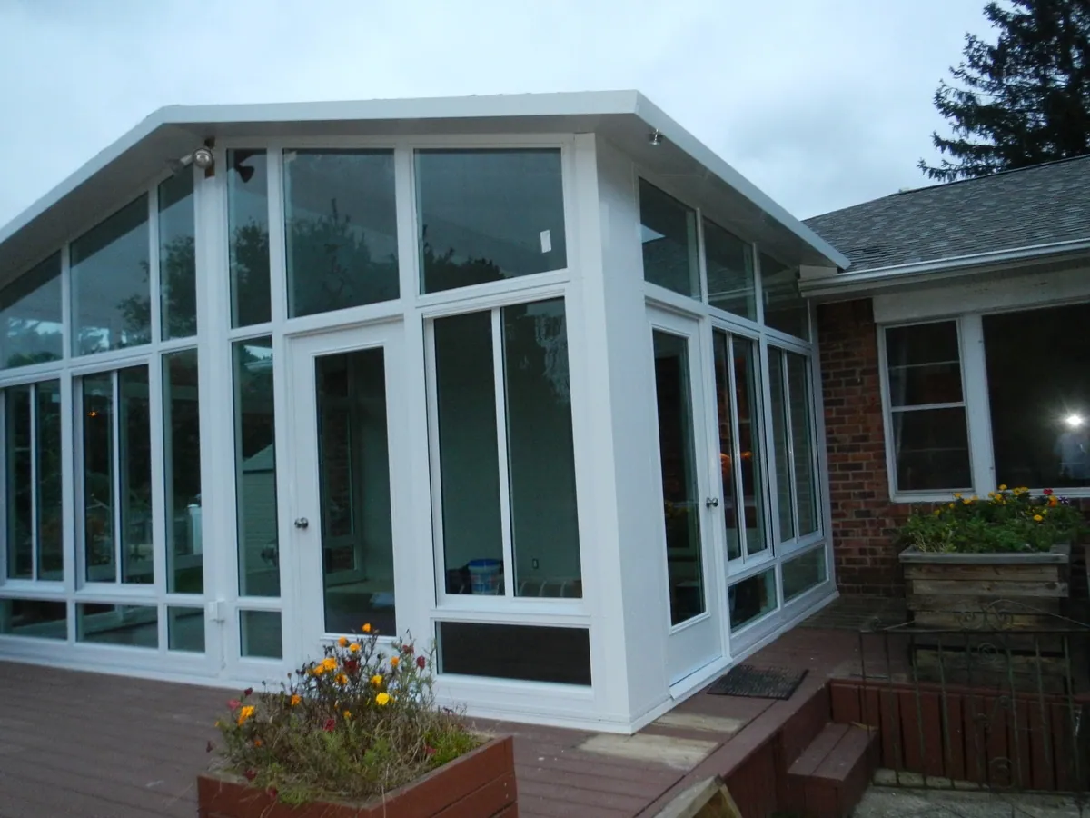 Tall white-framed sunroom with floor-to-ceiling glass beside a deck