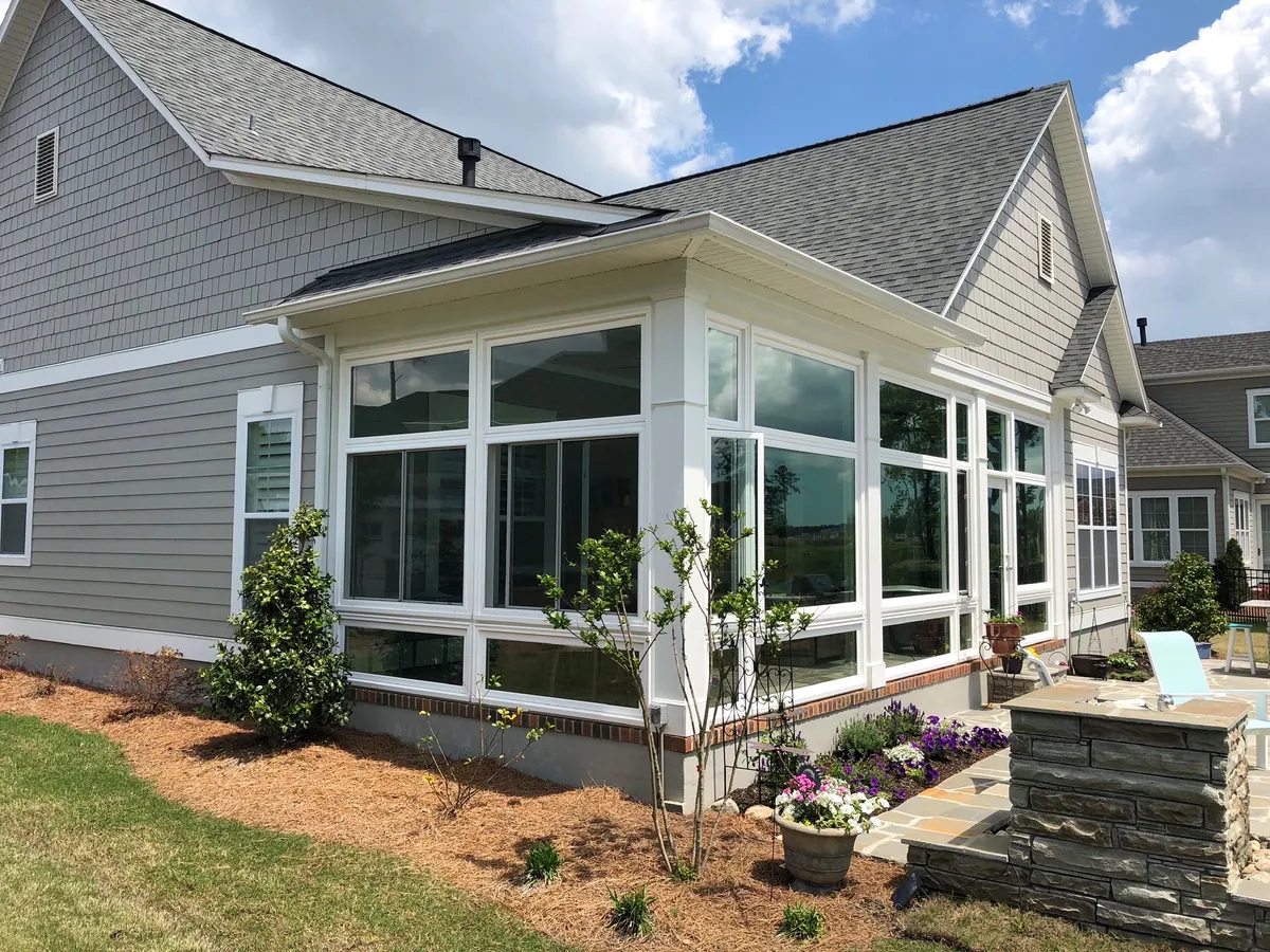 White sunroom on a grey-sided home with garden beds