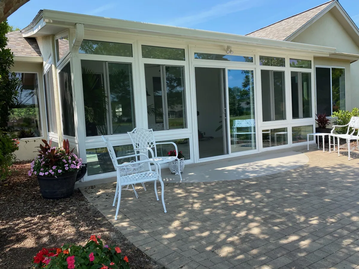 White sunroom opening onto a paver patio set with furniture