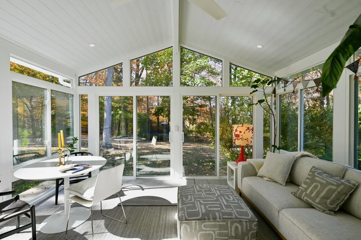 White cathedral sunroom with a sectional facing autumn trees