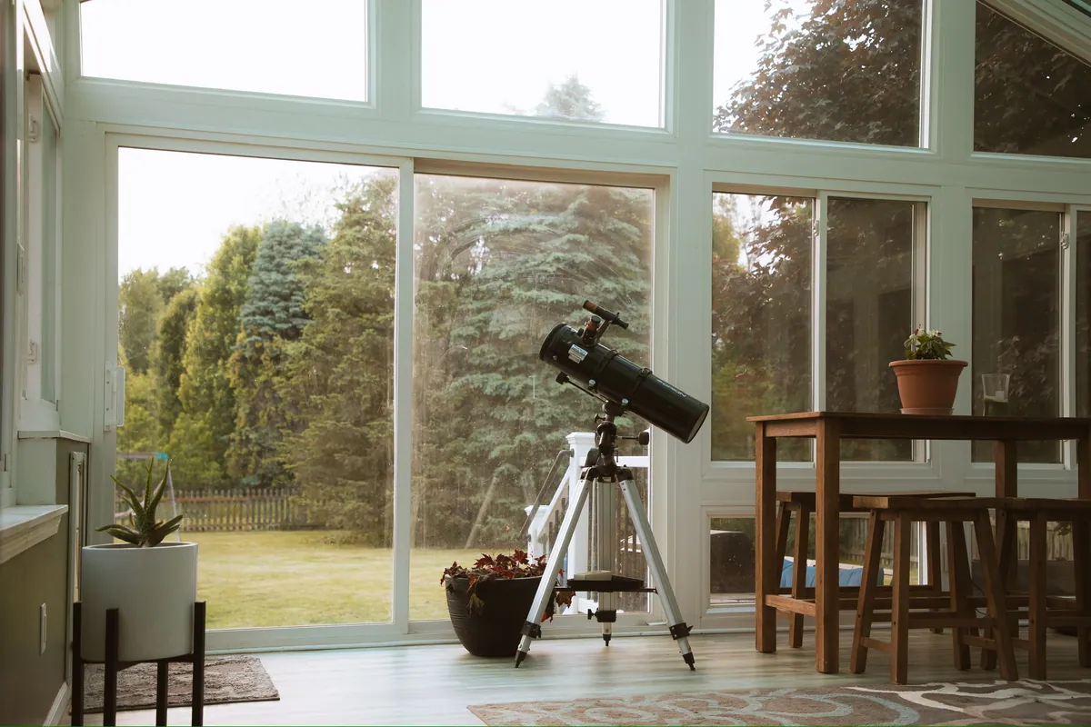 Sunroom with floor-to-ceiling glass and a telescope facing the trees