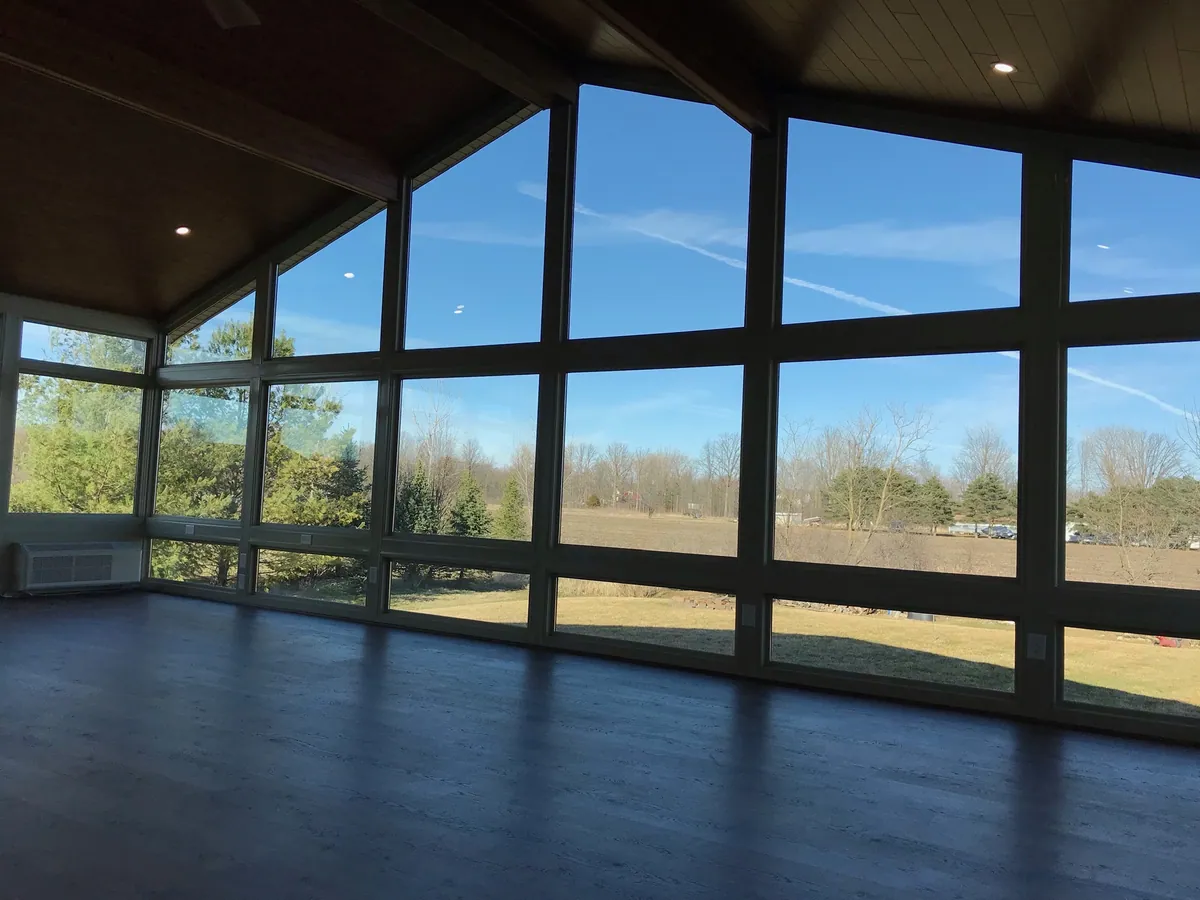 Black-framed sunroom at dusk looking over open fields