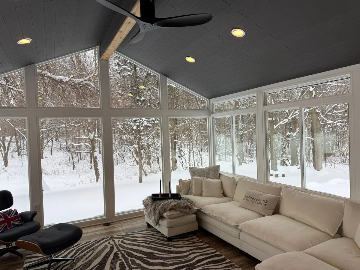 Grey-ceiling sunroom with a white sectional and snowy woods beyond