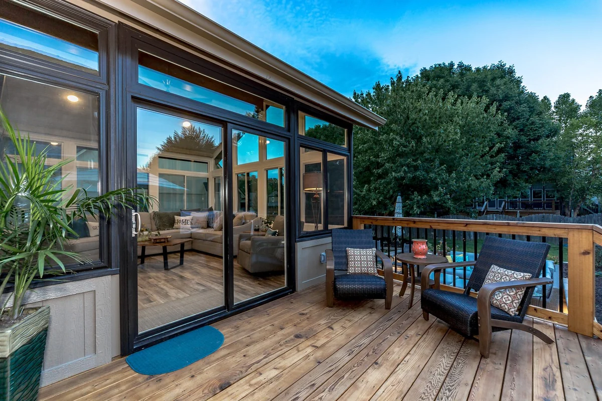 Three-season room at dusk, sliding doors open onto a cedar deck